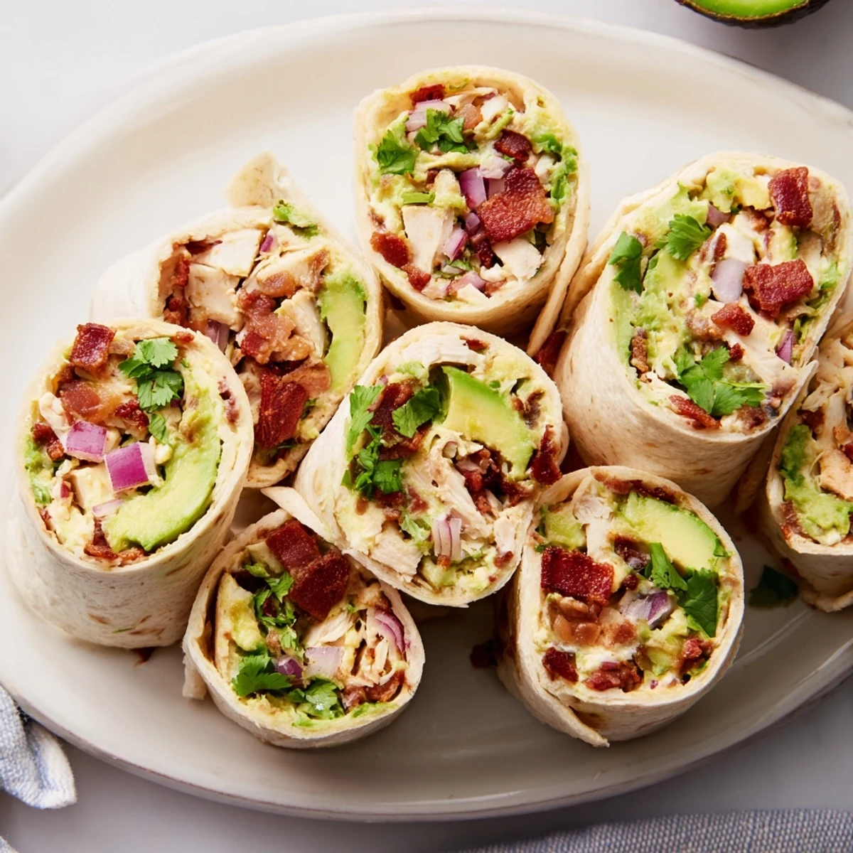 Creamy avocado chicken bacon pinwheels served on a cutting board, garnished with cilantro.  