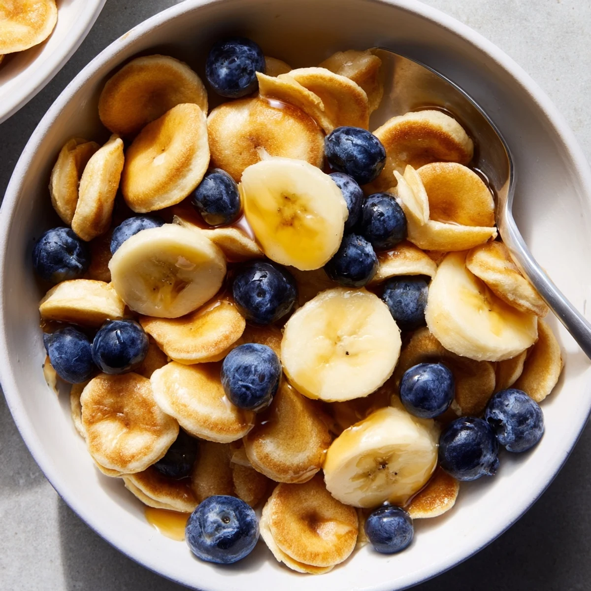 Mini Pancake Cereal served in a bowl with fresh berries and syrup drizzling over.  