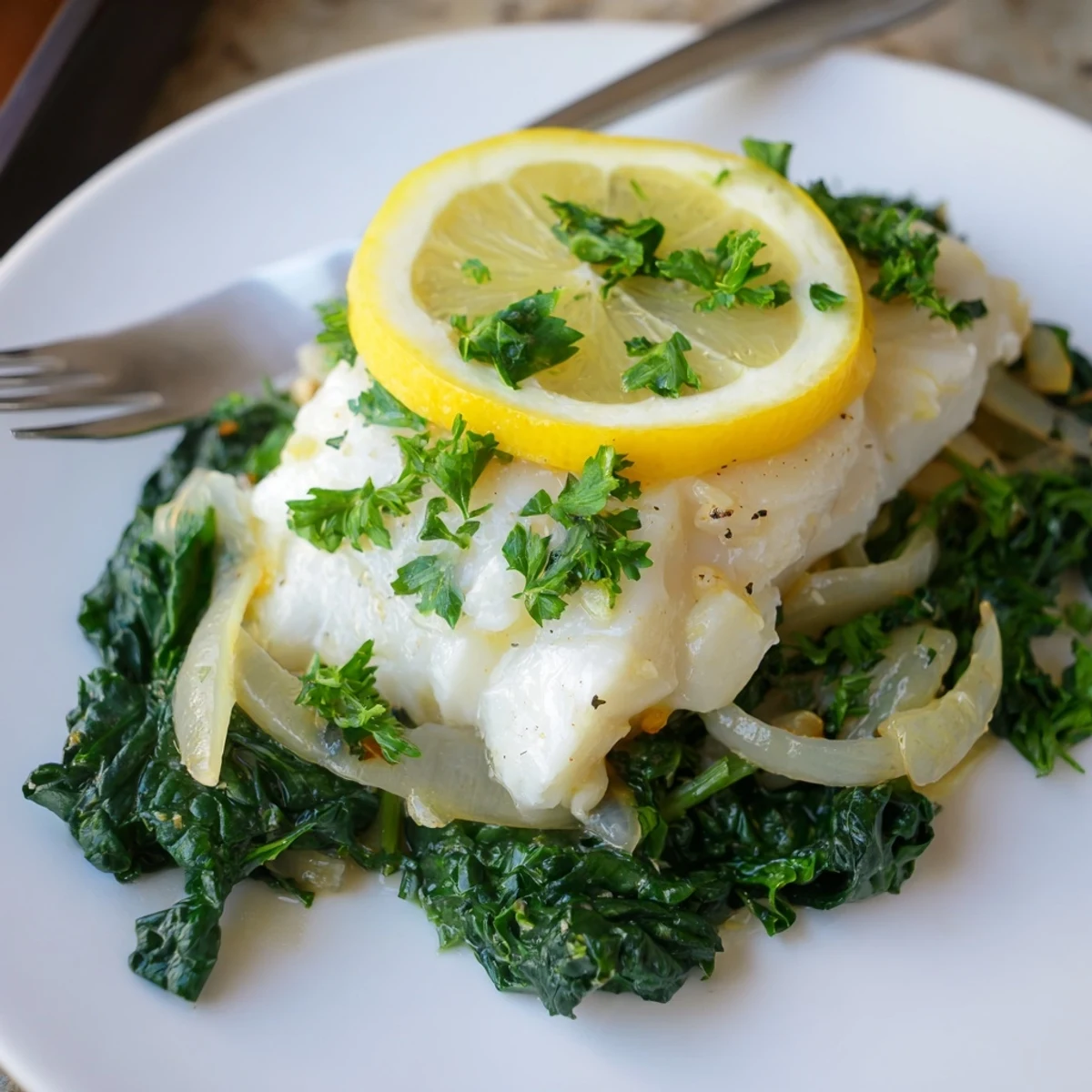 Tender lemon garlic baked cod served over vibrant greens, a healthy Mediterranean delight.  