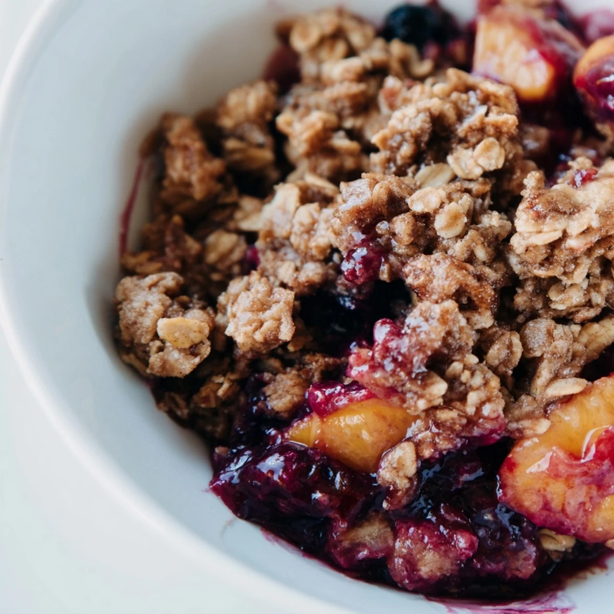 A close-up of a rustic Fruit Crisp featuring a mix of frozen fruit under a crunchy, oat-filled layer.