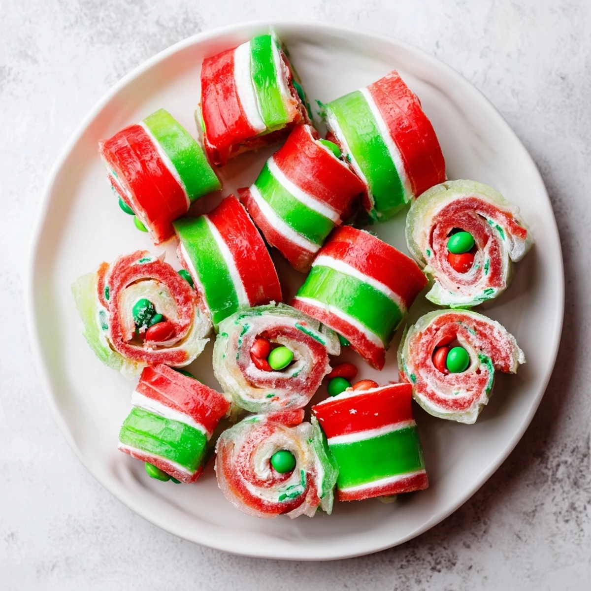Vibrant Easy Christmas Fruit Rollup Sushi rolls feature chewy fruit, marshmallows, and festive, colorful candies on display.