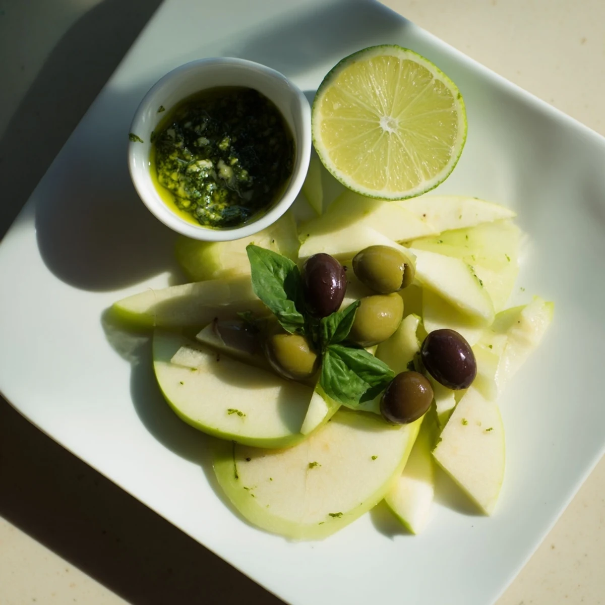 Delectable Emerald City snack board, showing green olives, cut limes, and a bowl of delicious pesto.