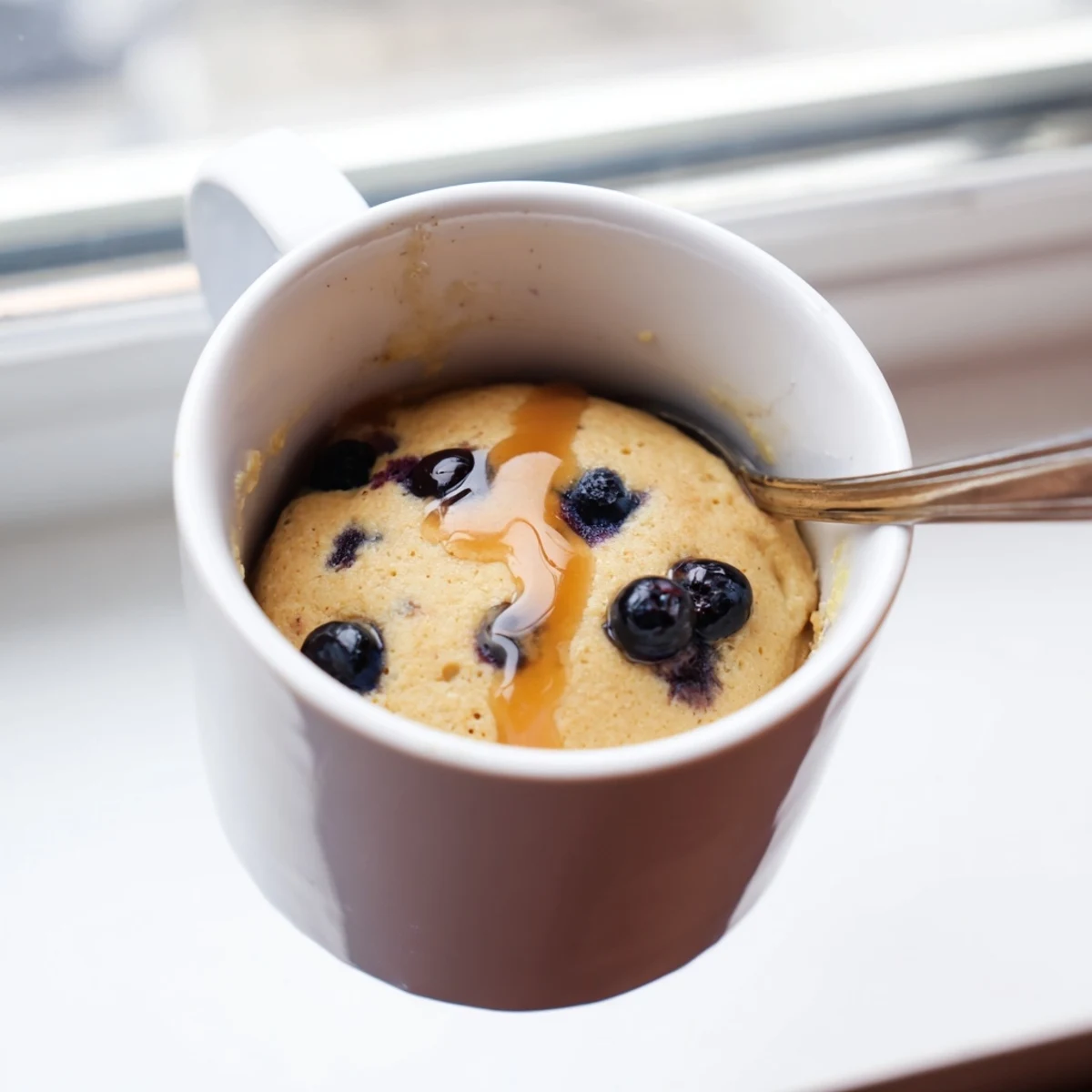 Indulge in a warm, freshly-made microwave mug pancake topped with fresh fruit like blueberries.