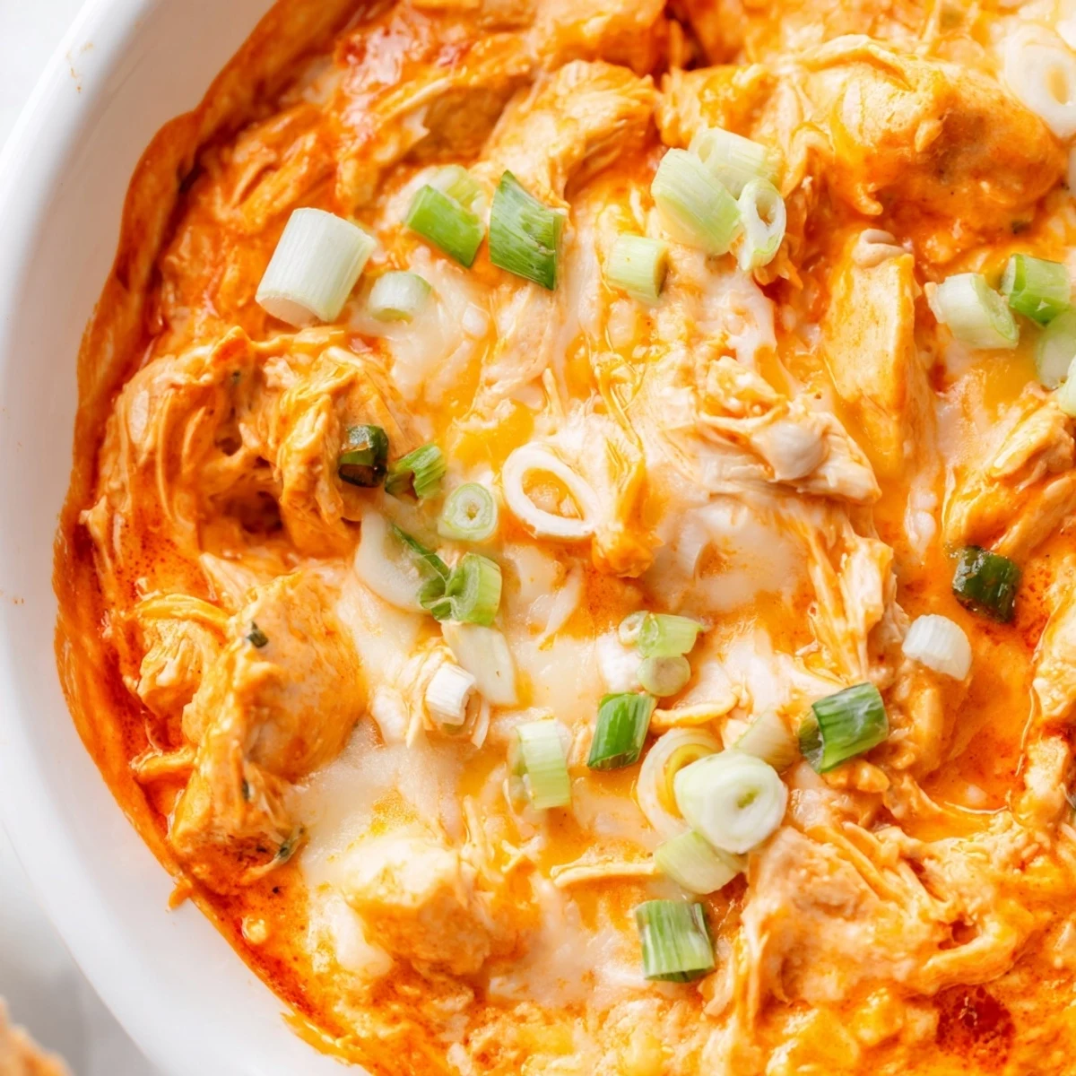 A bowl of warm, creamy Crock Pot Buffalo Chicken Dip is topped with melty cheddar and fresh scallions, ready for dipping.