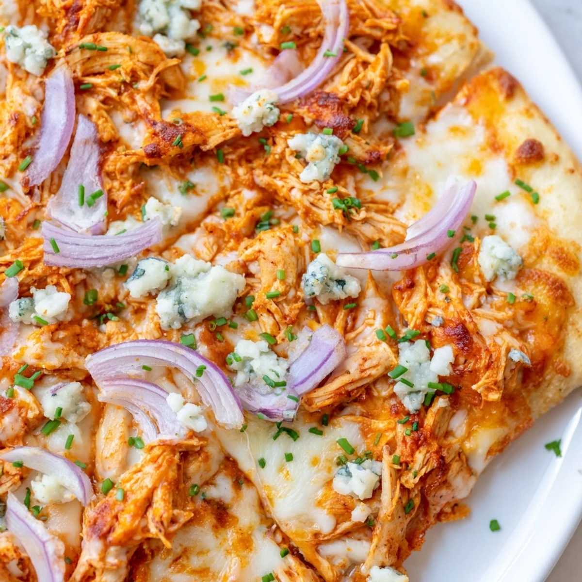 Golden-brown Buffalo Chicken Pizza fresh from the oven, topped with bubbly mozzarella, ranch drizzle, and fresh chives on a rustic cutting board.