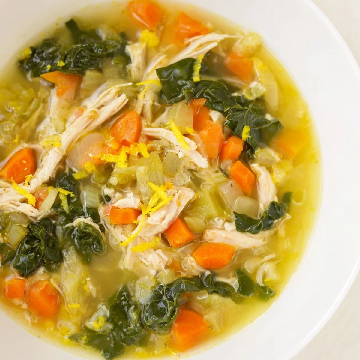 Close-up on High Protein Lemon and Turmeric Chicken Soup, featuring colorful carrots and celery, garnished with dill and a squeeze of fresh lemon.