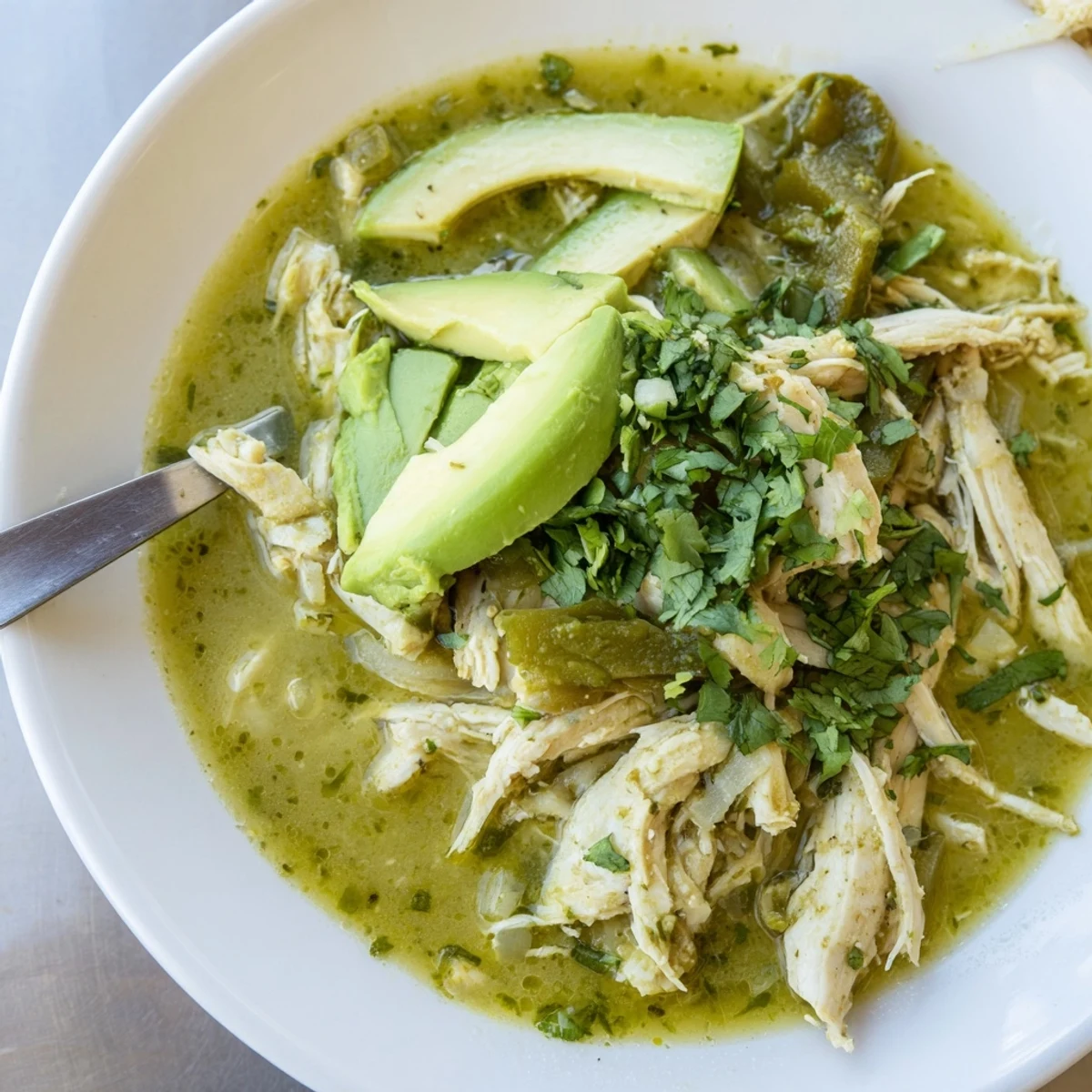 Close-up of Chicken Chili Verde in a rustic bowl, garnished with avocado and cilantro for a fresh finish.
