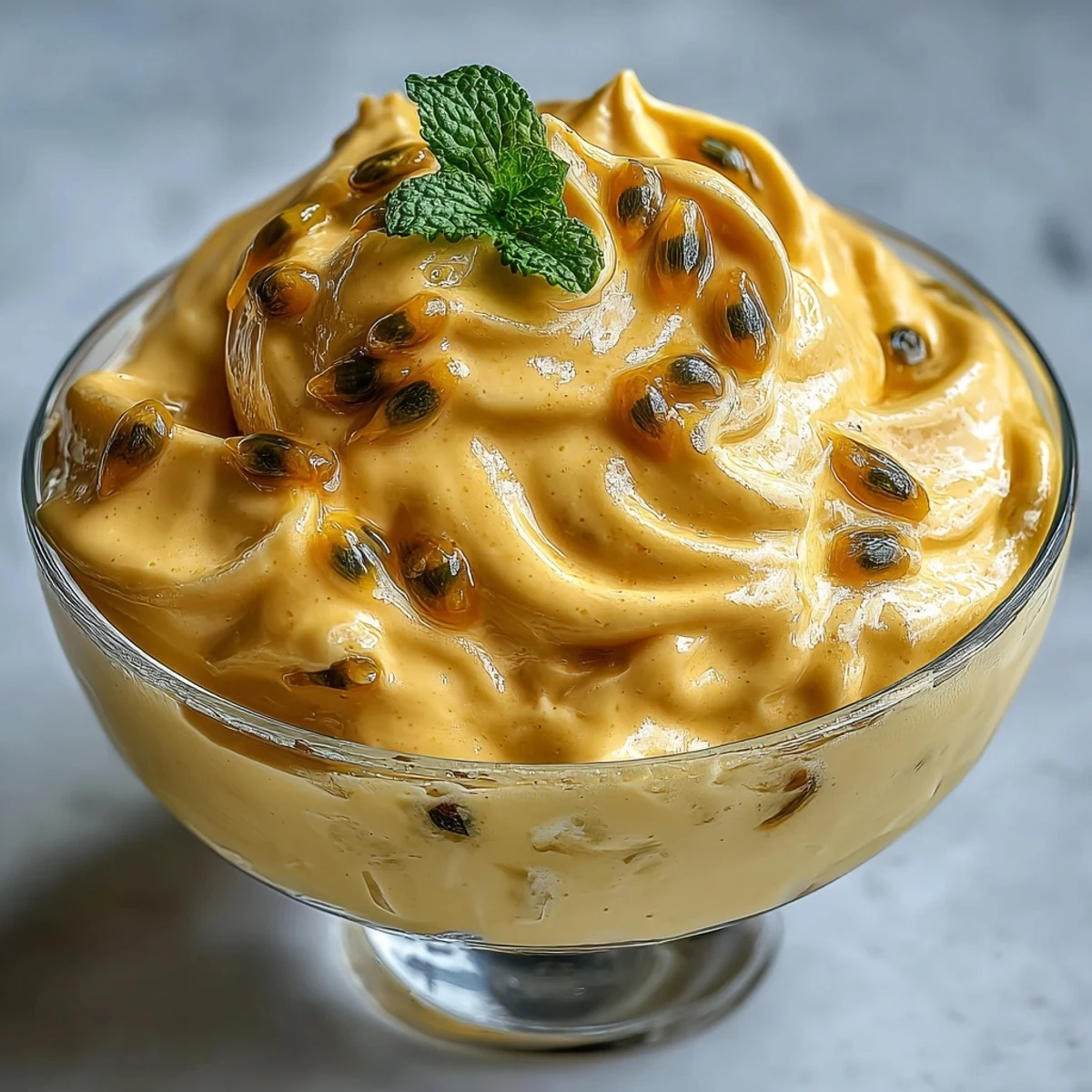 A spoon dips into fluffy Passionfruit Mousse, revealing an airy texture and vibrant yellow hue in a dessert cup.