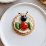 These Ladybug Love Picnic Finger Foods feature vibrant red tomatoes and black olive heads on crackers, ready to eat.