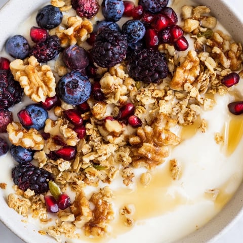 Creamy probiotic yogurt bowl topped with jewel-toned winter berries and a warm spiced crunch of cinnamon and ginger.