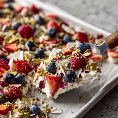 A spoon is scooping up a dessert with strawberries and blueberries.