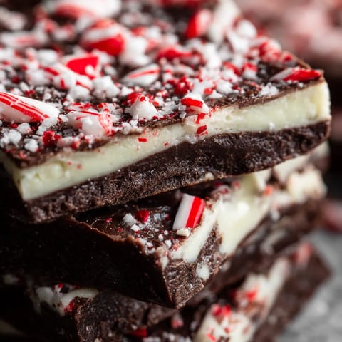 A stack of chocolate cake with white frosting and red and green sprinkles.