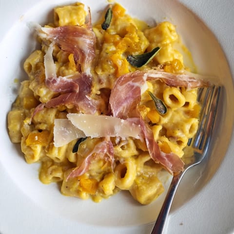 A close-up of creamy Roasted Pumpkin Pasta with Crispy Prosciutto, topped with fried sage.