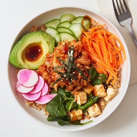 Colorful bowl of grains and vegetables, featuring homemade kimchi and avocado slices.  