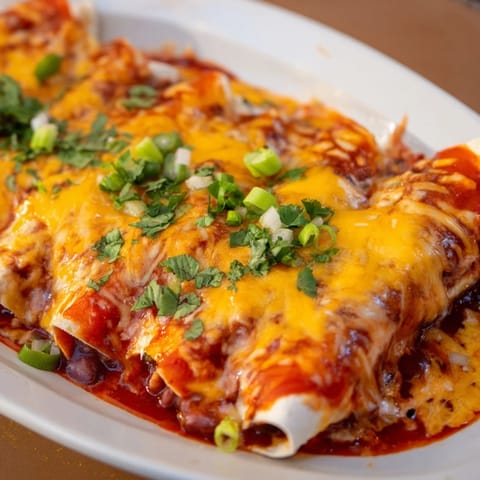 A close-up of a baking dish full of incredibly cheesy Cheesy Bean Enchiladas, garnished with fresh cilantro.