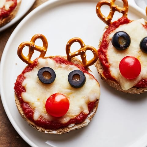 Homemade Reindeer Face Pizza Bagels feature melted cheese and pretzel antlers, perfect for kids.