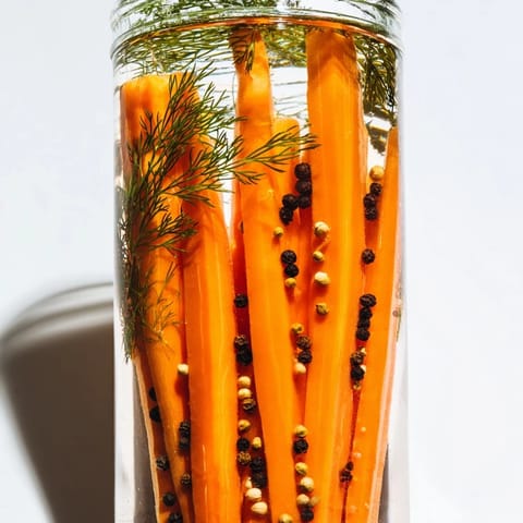 Bright orange quick pickled carrot spears with garlic and spices, ready to chill for zesty flavor.
