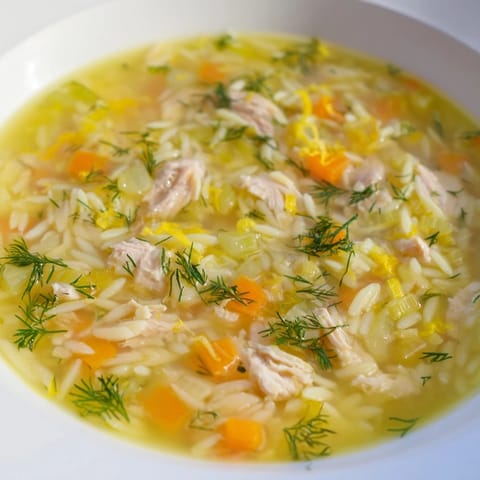 Close-up of a flavorful bowl of Chicken Lemon Orzo Soup with chunks of cooked chicken.