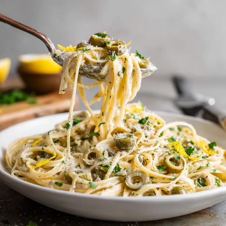 A fork is being used to eat spaghetti with a green olive on top.