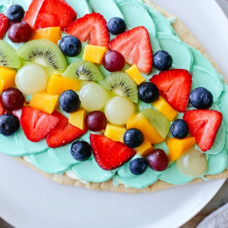 Fresh fruit decorates a creamy frosting on the finished Under the Sea: Mermaid Tail Fruit Pizza dessert, a festive treat.