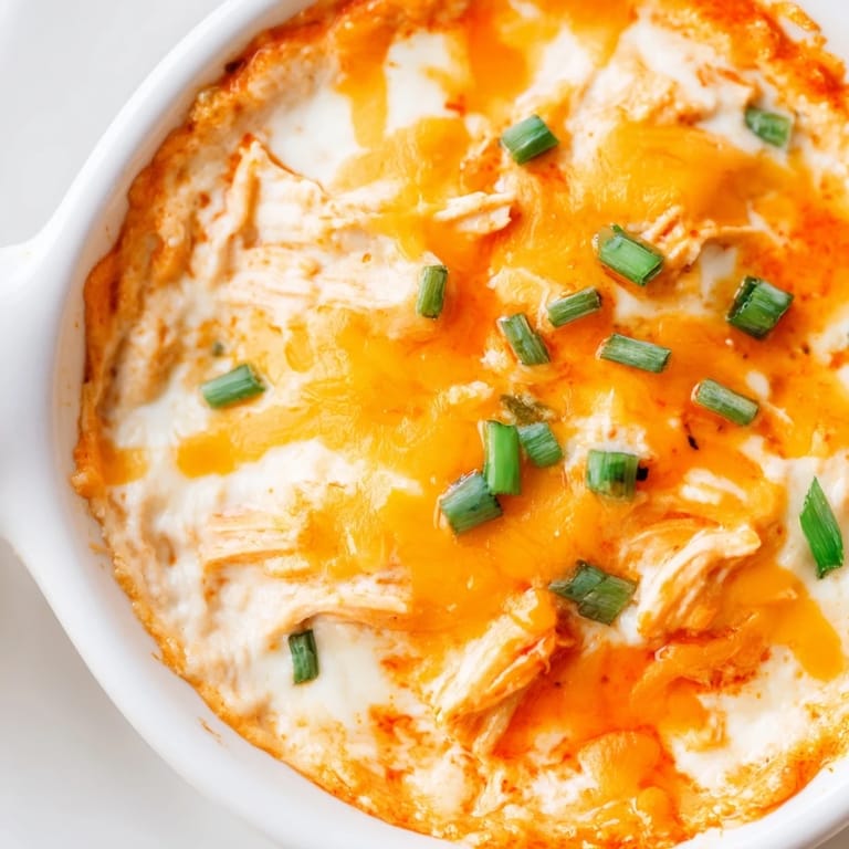 A golden, baked version of Crock Pot Buffalo Chicken Dip in a serving dish, garnished with extra cheese and served with tortilla chips.
