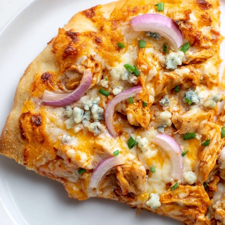 Close-up of Buffalo Chicken Pizza with melted cheese and ranch drizzle, served on a white plate with celery sticks on the side.
