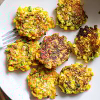 Crispy sweet corn and zucchini fritters served on a rustic plate with herbs.