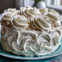 First Communion Cake with White Roses and Cross Topper on a white cake stand, elegant vanilla sponge layers with silky buttercream and delicate fondant roses, crowned with a decorative cross topper.